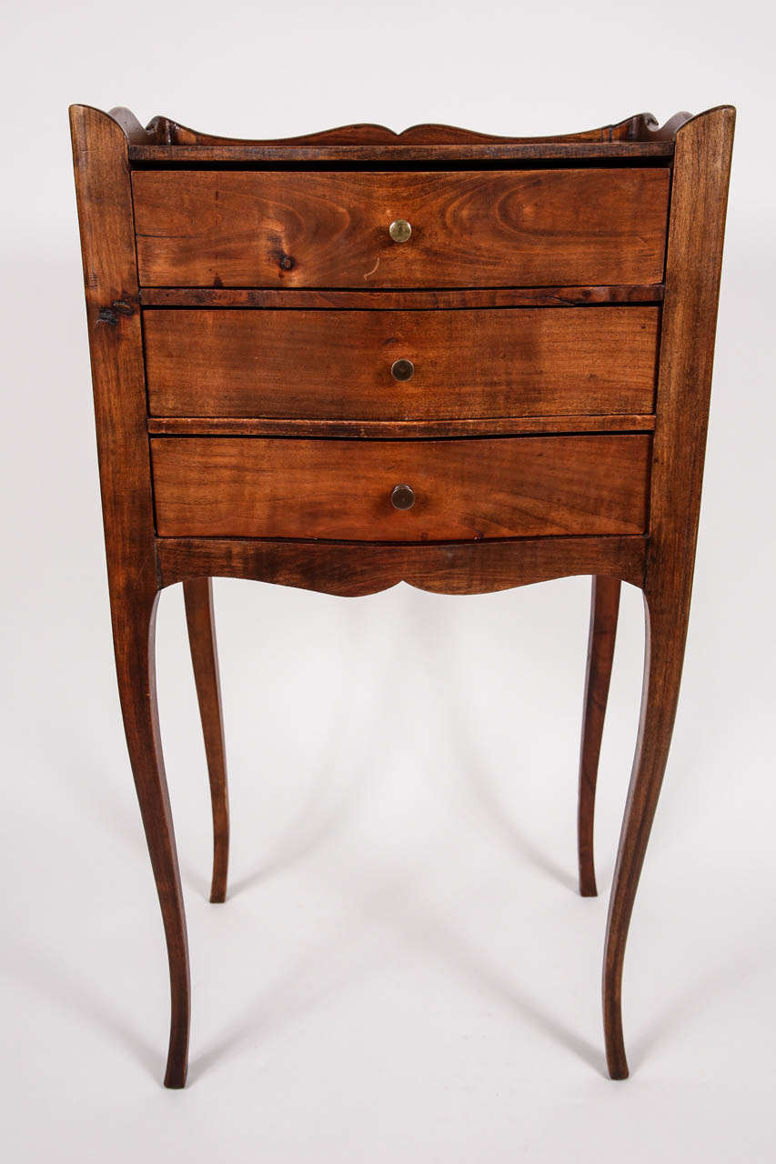 Turn of the century French bedside table. Table has three drawers with brass knobs and features legs in the cabriole style. French, c. 1900s
