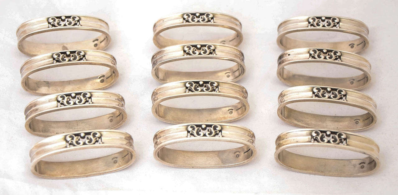 A set of 12 sterling silver napkin rings made by the firm of Georg Jensen and designed by Johan Rohde. These 12 oval, scroll-pattern rings were made in Copenhagen post 1945.
