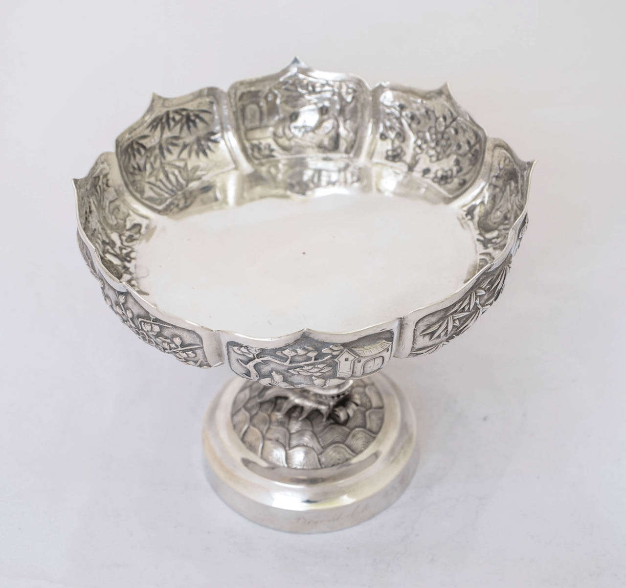 A Chinese export silver tazza made by Wing Chun of Hong Kong, circa 1900. The shaped circular dish is variously embossed with figural scenes, bamboo, prunus and dragons; and is supported by a single dragon.
The tazza is 13.3 cm high; the diameter