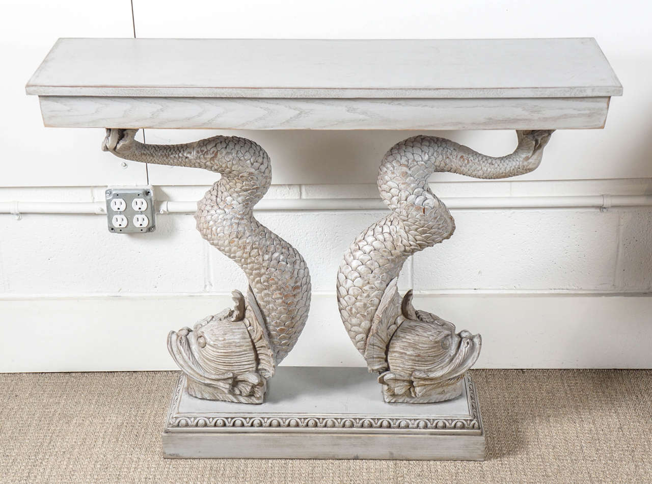 Here is a beautiful carved wood console with a double dolphin base.
The finish is in a cerused gray wash with intricate carved detail throughout.