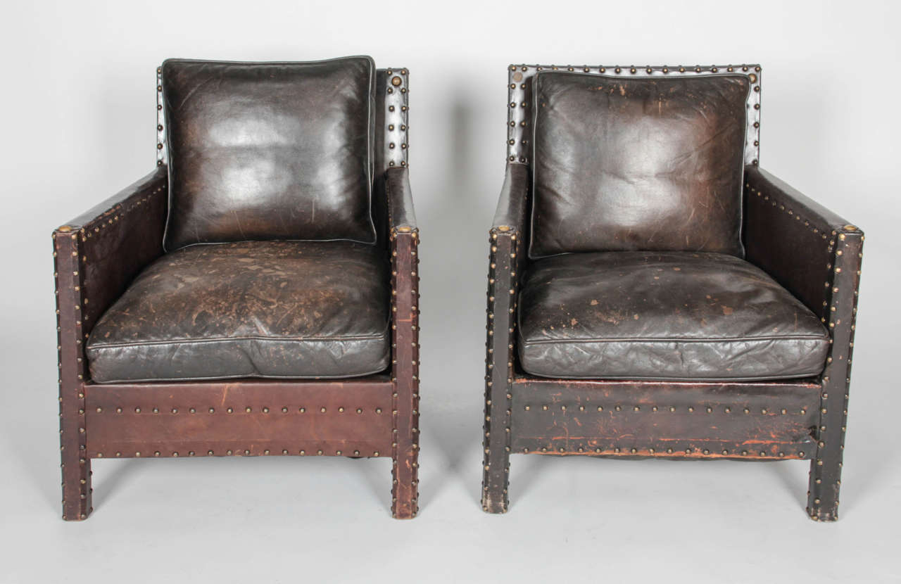 Very structural pair of arm chairs from the early 20th century. Nailhead trim along edges of arms, seat, and backrest adds an industrial quality. Possible Spanish Revival influence. Leather detail on chair extends to wrap front legs. Seat cushion