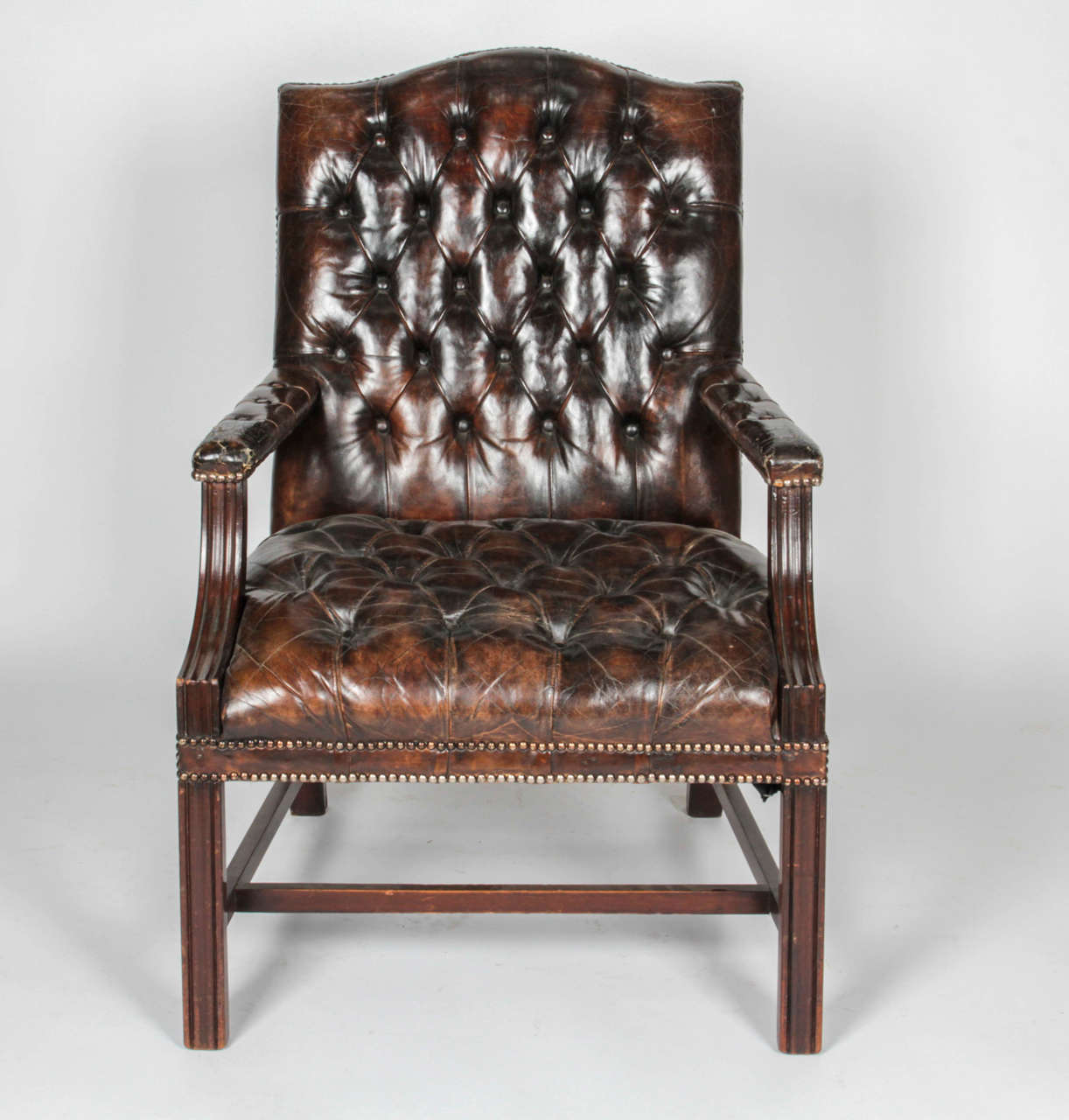 Pair of leather armchairs with wooden legs and stretcher. Done in the Chesterfield style. Brown leather appears to be original and more worn along the seat front with cracking on the arms (see pictures). nailhead detailing along edges.

Not