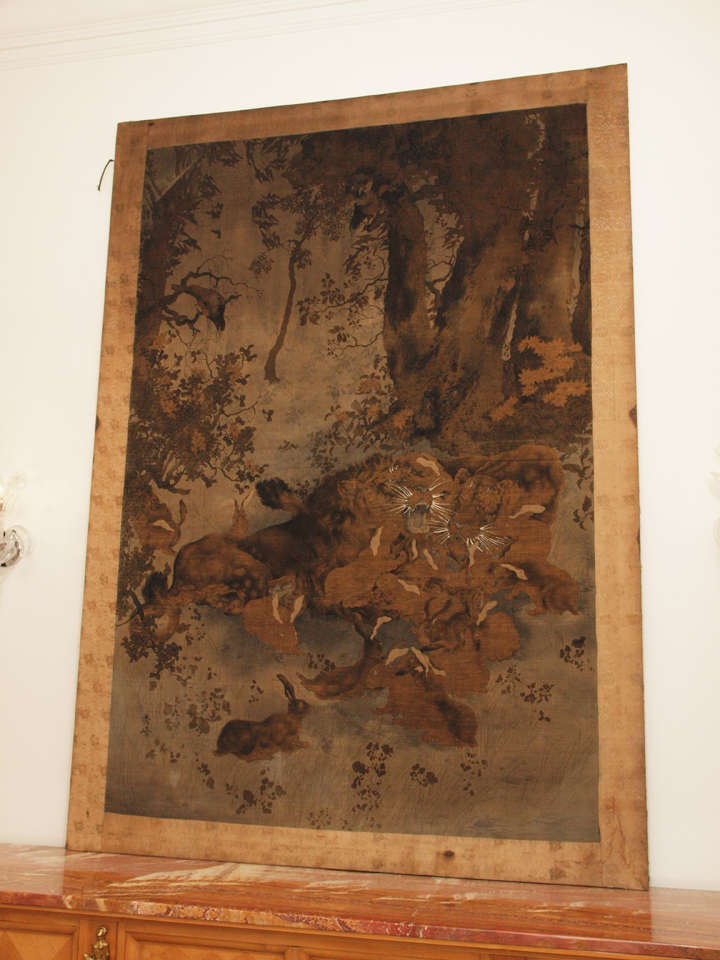 Beautifully detailed landscape in bronze tones on antique silk with roaring lions and docile rabbits; wooden stretcher