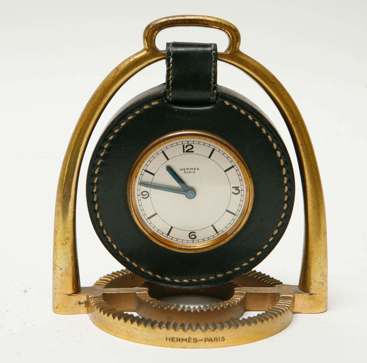 A leather and brass stirrup clock designed by Paul Dupre Lafon for Hermès. The circular base has an indented ribbed design topped by an arch, depicting a stylized stirrup, from which hangs a round clock with Swiss movement and a black leather frame