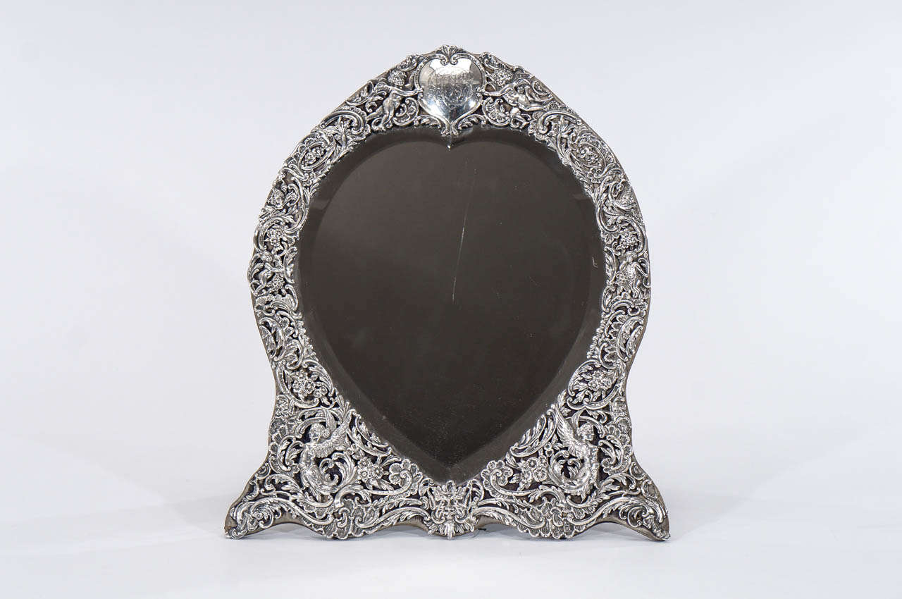 This is a rare and extremely large 19th c. English sterling silver frame with 
all-over filigree work depicting Neoclassical motifs. Mounted on a velvet stand, the frame is cut out in a stylized heart shape with a central reserve of a heart shaped