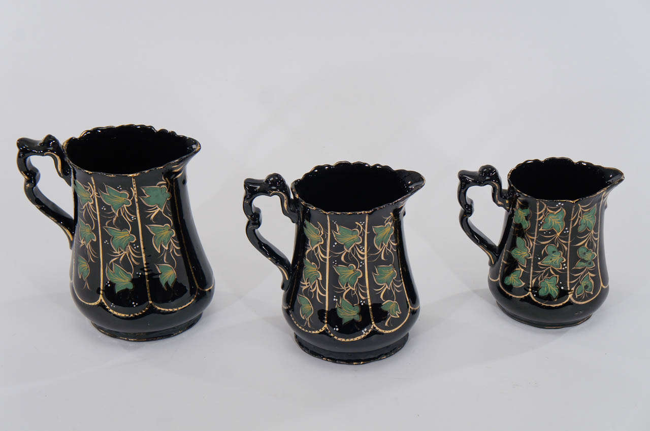 This rare and wonderful decorative set of three matching Jackfield pitchers with hand-painted ivy leaves along the body is in perfectly graduated sizes. The black ground contrasts beautifully with the green enamel leaves, all highlighted with gold.