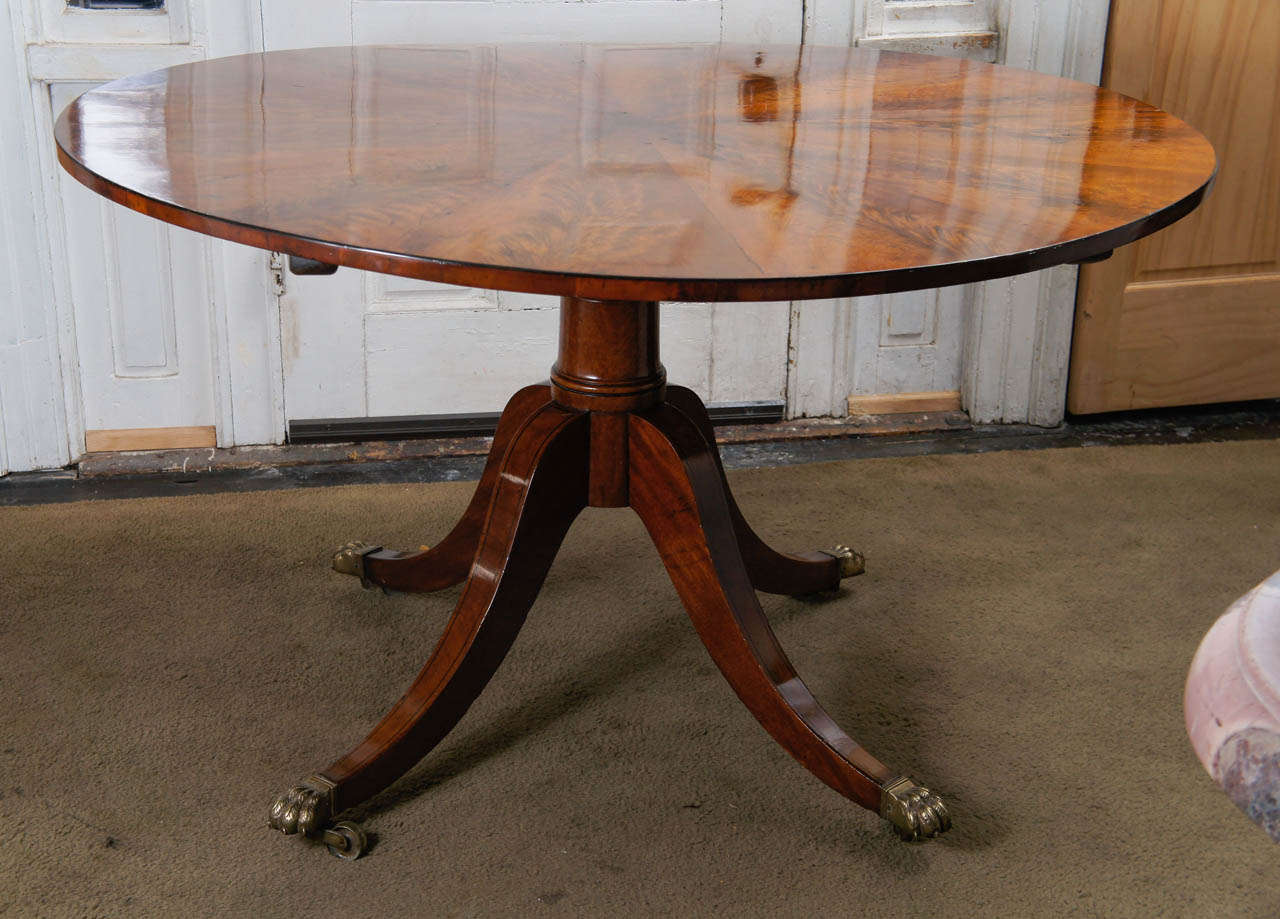 This period regency table shows a top centered on pie shaped wedges of veneer in a fine dramatic flaming creating an expanding pattern terminating with a simple but rich ebony string line inlay border. Centered on  a finely balanced and turned
