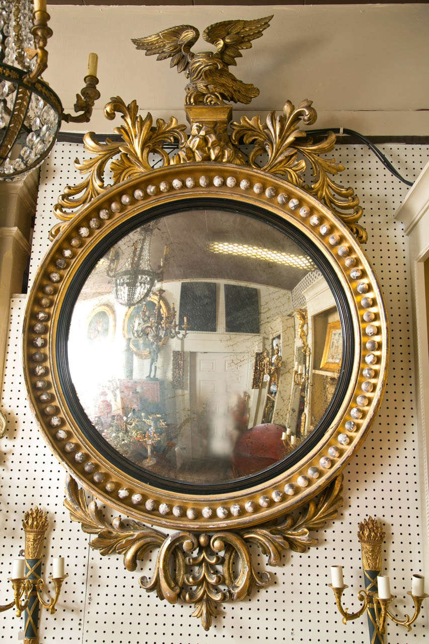 Either English or American this large convex mirror is topped by a spread wing  eagle on a rocky base surrounded by foliate carvings. The mirror itself is surrounded by many balls and blackened wood bezel. The bottom has more carved foliates.  