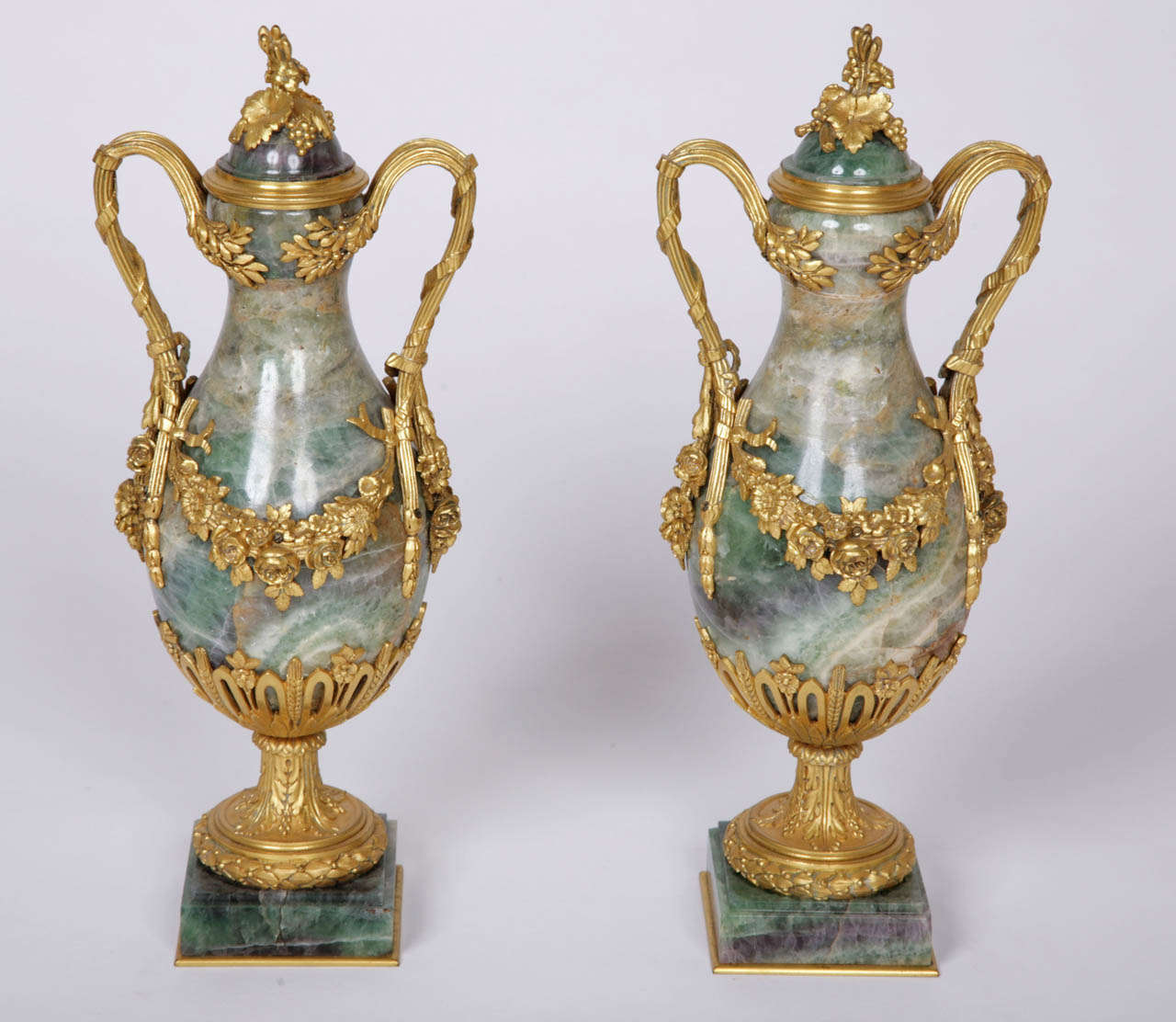 The baluster form fluorspar vases on square pedestals, decorated with ormolu mounts in the form of twin-handles and garlands of flowers and grapes