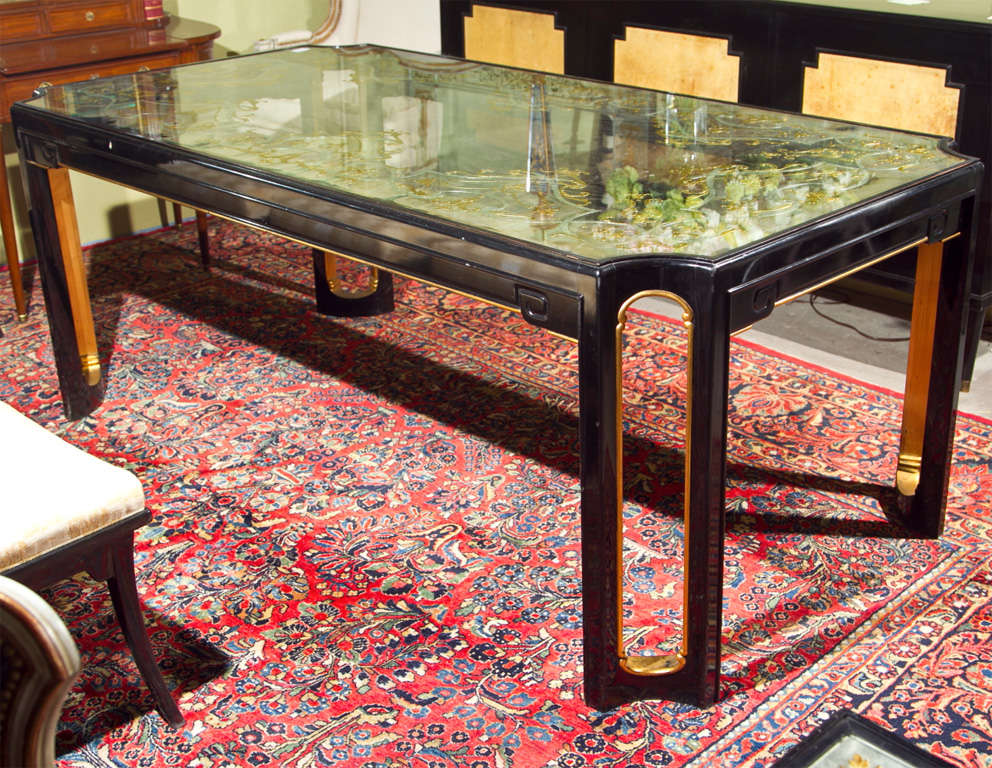 A truly unique and glamorous dining table by Maison Jansen, circa 1940s, the beautiful verre eglomise glass top inset in an ebonized and parcel-gilt base, in the style of Hollywood Regency. Please see the dining chairs in a separate listing.