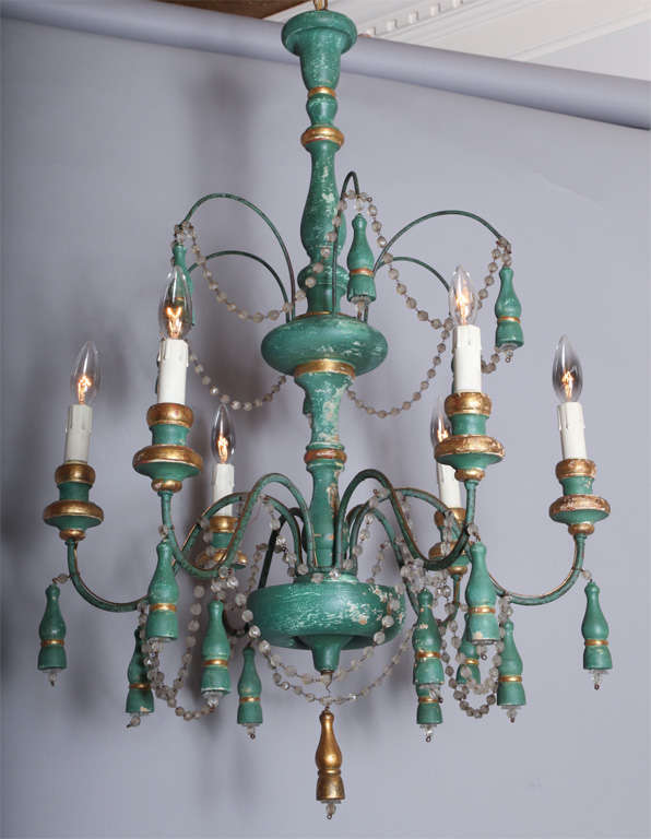 Two tiered chandelier, having turned wood center column, painted green with gilt accents; six S-curved iron candlearms with wood candlepots, each arm adorned by a wooden tassel finished by a glass bead, and draped with strings of glass beads.