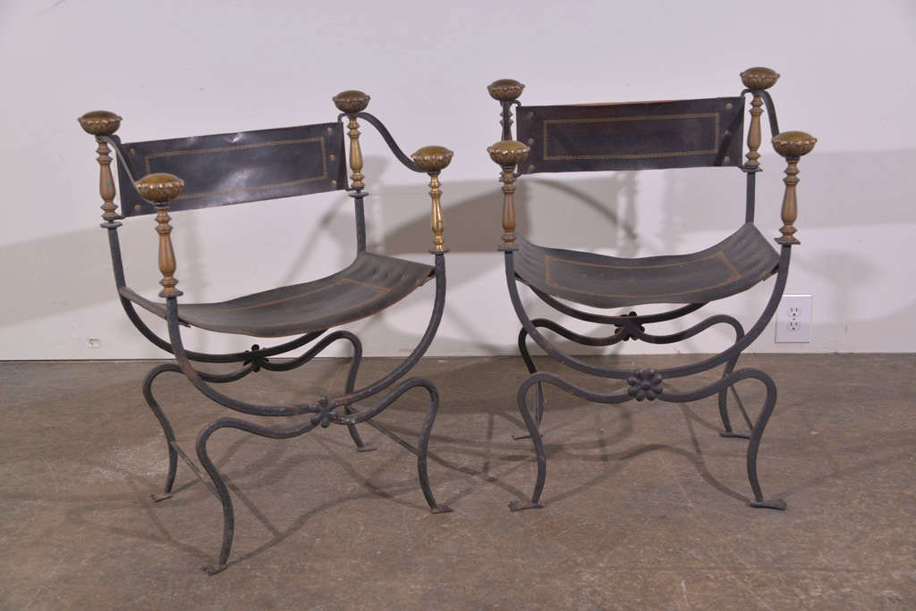  Pair of brass and wrought iron campaign chair with overscaled finials and gilt leather seat and back circa 1940. 