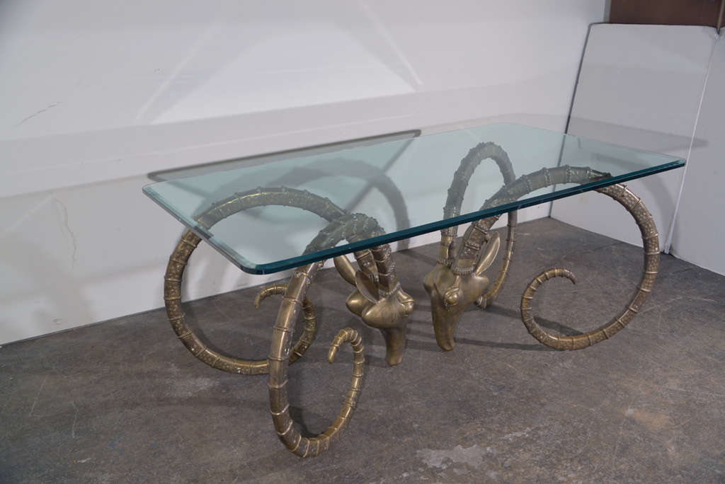 Iconic polished brass rams head dining table with glass top. Glass measures 72 x 40 x .5 and has curved corners and beveled edge.