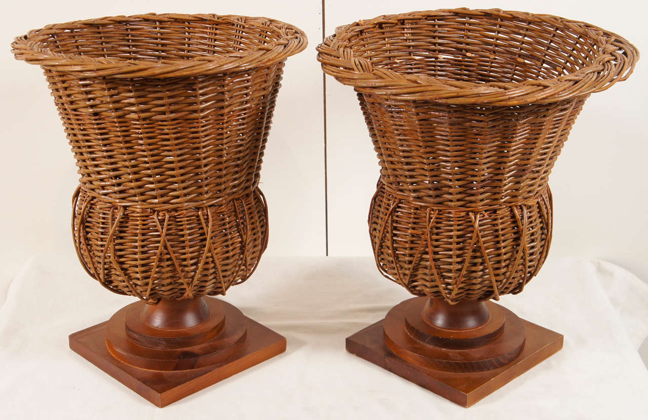 Here is a pair of wicker urns with wooden pedestal bases in a walnut finish.