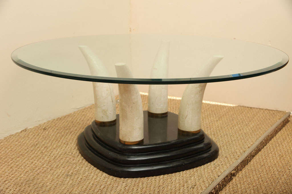 This cocktail table is anchored by a substantial dual-tone tessellated stone base. Three tears lead up to the four off white stone tusks. The brass rings are on the bottom of the four tusks. The glass is original and has a few minor scratches and