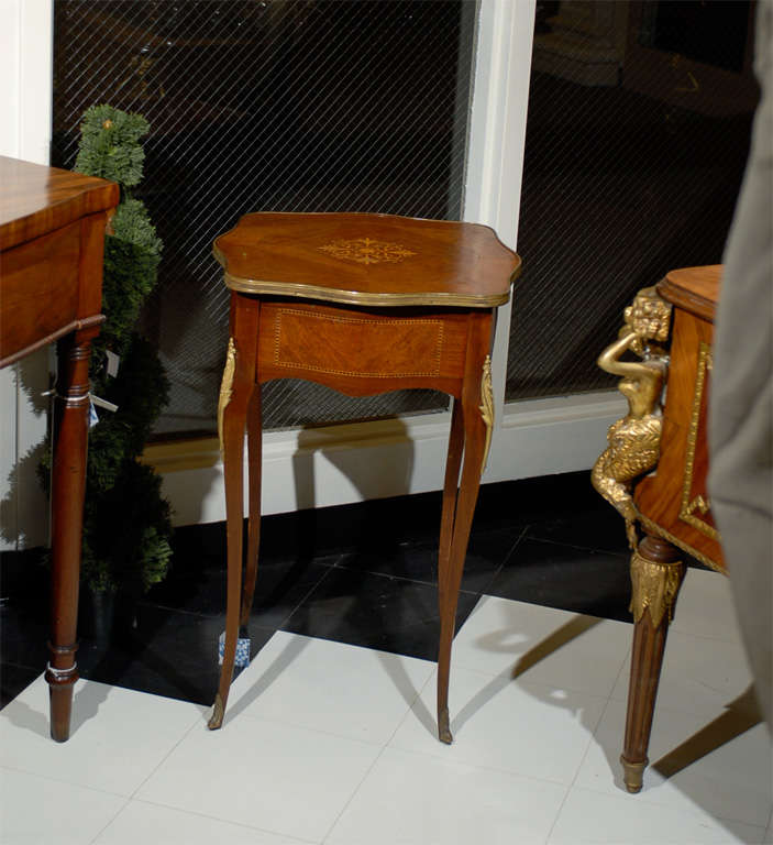 Early 20th Century side table of rosewood, mahogany, satinwood, and ebony.  The shaped top is trimmed in brass ormolu and has a bookplate veneer centered by a marquetry inlay of satinwood.  The aprons are serpentined on all sides and have a