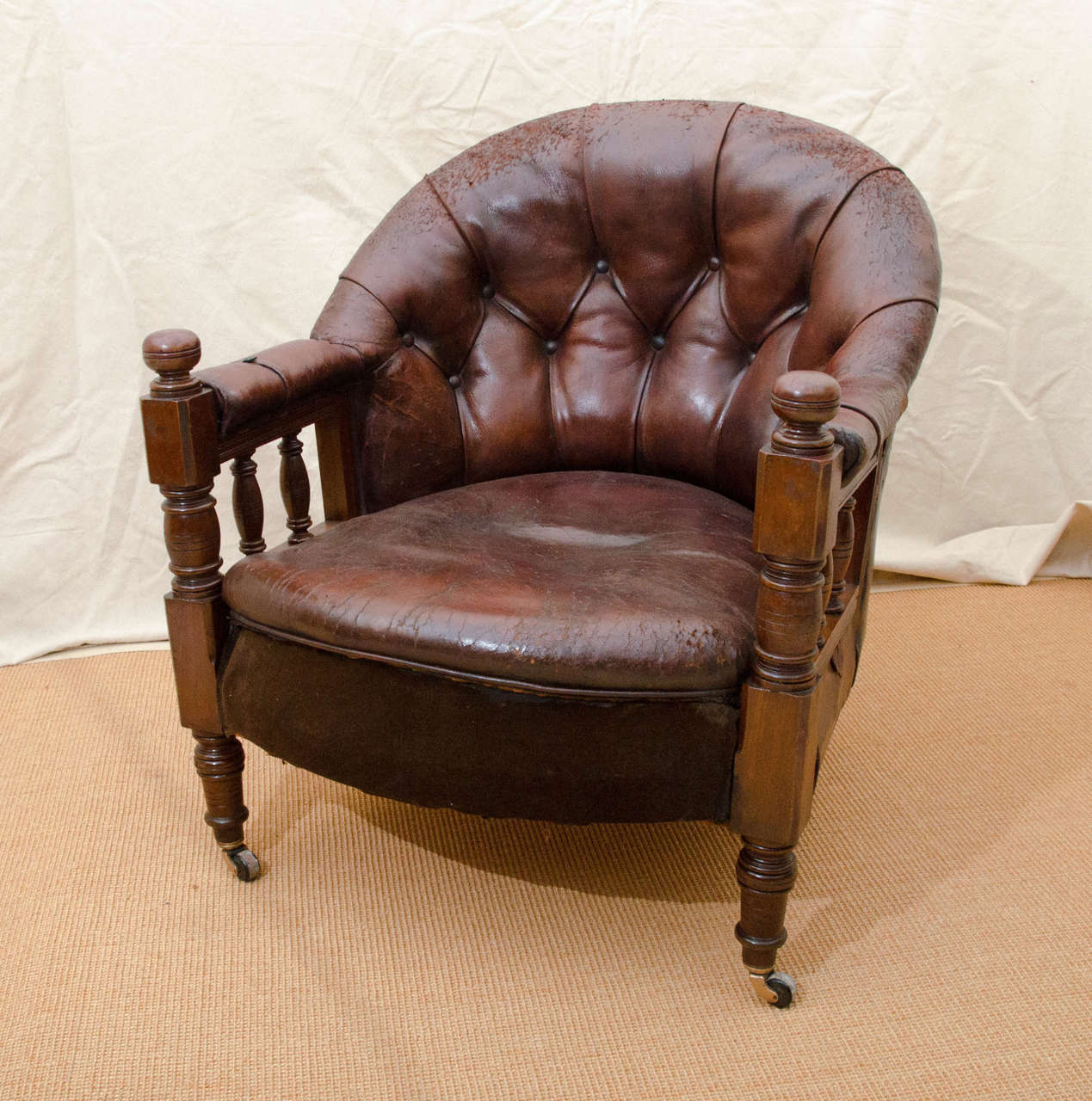 English Victorian tufted leather barrel back spindle support open armchair. The chair is mahogany framed with turned front and rear legs on brass castors having brown ceramic wheels. The bottom front of the seat has been replaced with dark brown