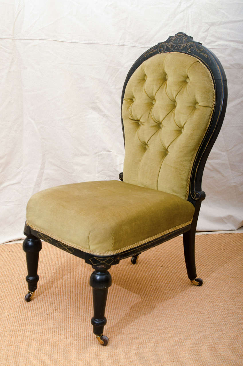 English Victorian ebonized tufted back slipper chair with incised gilt decoration, the incising is Eastlake influenced. The legs end with brass castors having black porcelain wheels.