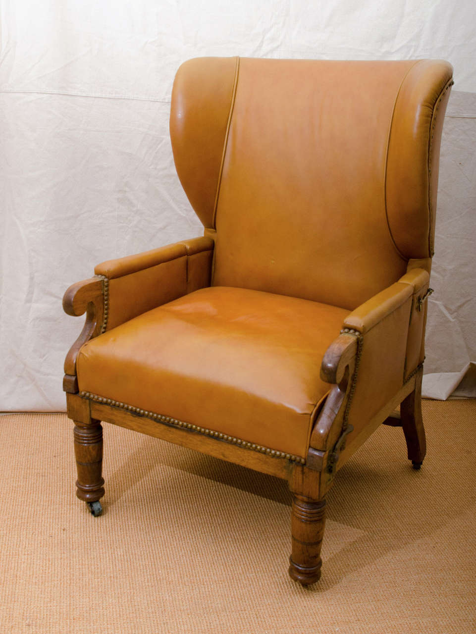 English early 19th century leather covered invalid's wing chair. The chair adjusts and the arms fold out by lifting up brass levers at each front side. The back has brass hooks on each side that when released lets the back recline (see image 6 and