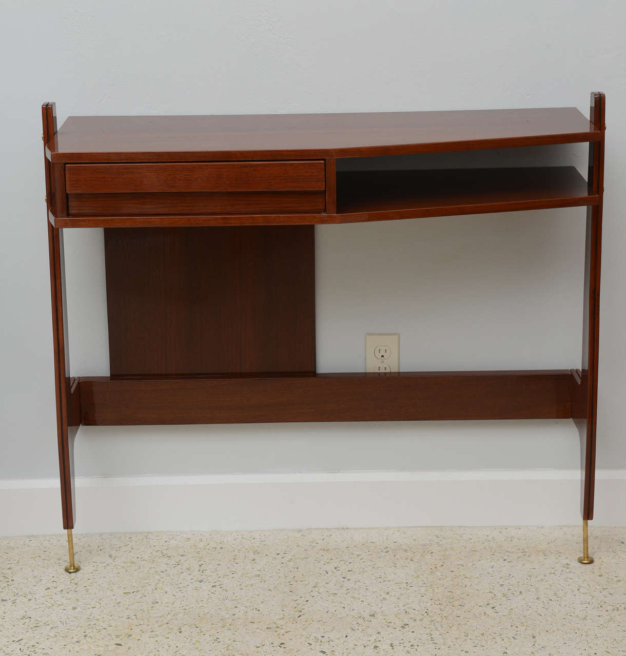 The shaped top above a drawer with a fin pull and conforming lower shelf, with partial back plate and cross stretcher, on brass legs, with tapering legs.