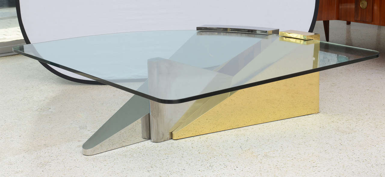 The shaped glass top cantilevered above a sculptural base made of polished harass, chrome and stainless elements.