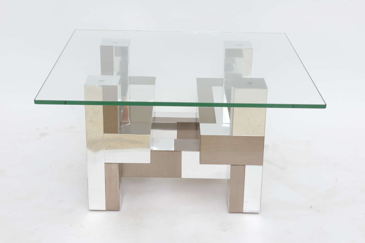 The square glass top above a geometric base in cityscape pattern with chrome and pewter tones, signed Paul Evans.
