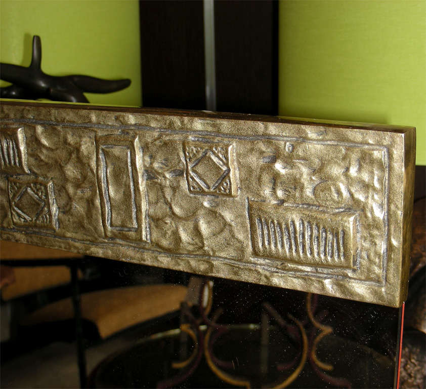 The mirror has a bronze border at the top and bottom, embossed with geometric cartouches.