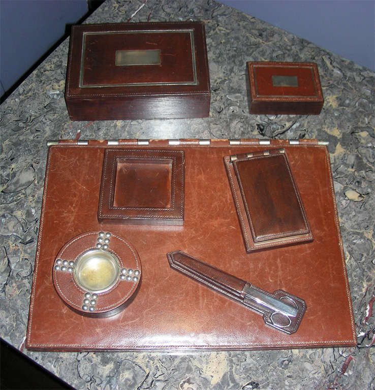 Made with brown stitched leather these accessories consist of a blotter, scissors + letter opener with case, two rectangular boxes, a square ashtray and a note pad.  All items are signed Hermes. The bloter measures 41 cm by 55 cm.