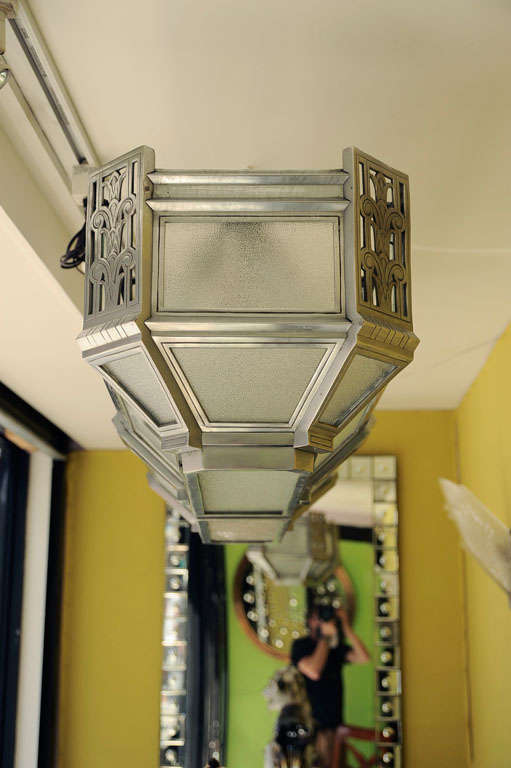 An American skyscraper Deco flush-mounted ceiling fixture, the rectangular silvered bronze frame with squared corners having vertical elements with pierced fret, stylized floral motifs, the underside with two hinged panels. Two available.
 