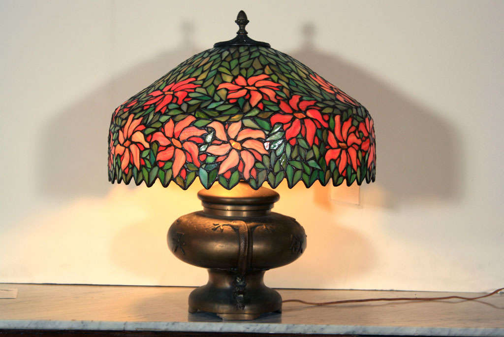 An extremely attractive and finely made antique poinsetta leaded glass lamp shade, consists of vivid orange, green, & coral color, stands on a decorative bronze oriental base, base not original. This one of a kind shade is 12
