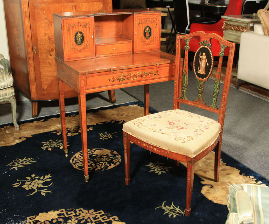 A petite Adam style paint decorated desk with pull-out table top, and a matching chair with paint decorated medallion back splat, upholstered in burlap. Desk $3300, chair $1750. Chair measures 36H, 20W, 16D.