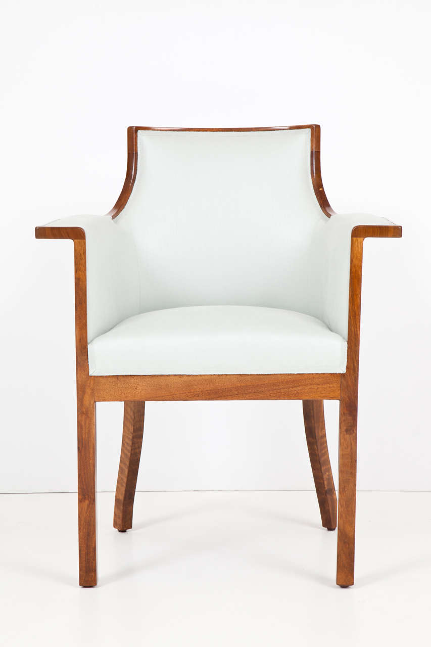 An Austrian walnut and upholstered armchair, Circa 1900, with a curved backrest, downswept partially padded armrests raised on straight supports, tight upholstered seat raised on square legs.
