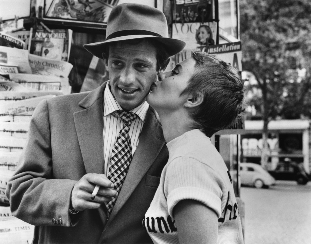Raymond Cauchetier Black and White Photograph - Jean-Paul Belmondo and Jean Seberg kiss in front of a kiosk