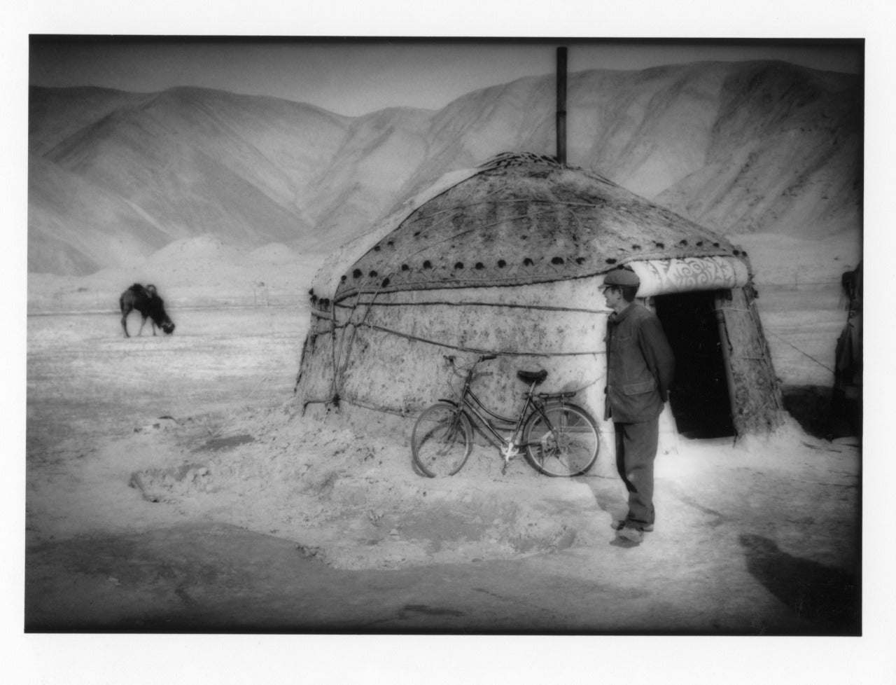 James Whitlow Delano Black and White Photograph - Kyrgyz herdsman watches his camels from outside his yurt, LandscChinese Turkesta