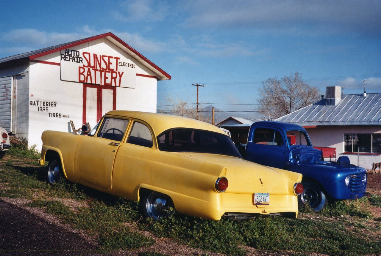 Kingman, Arizona von David Graham ist ein 20 x 24 Zoll großer C-Print, erhältlich in einer Auflage von 25 Stück. Dieses Foto zeigt einen gelben und einen blauen Wagen vor einem weißen Schuppen. Dieses Foto ist signiert, betitelt, datiert und