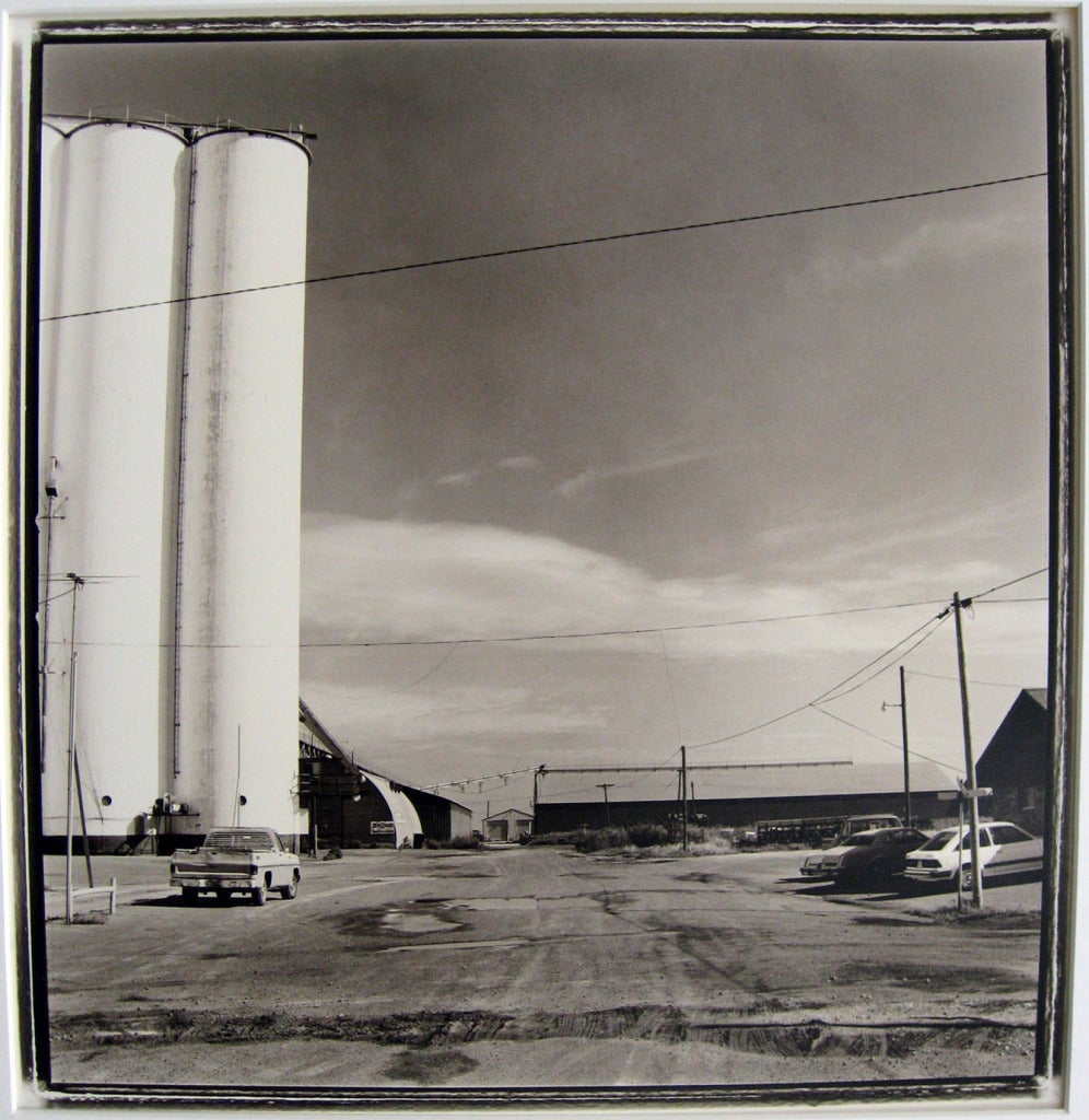 Happy, TX by Keith Carter is a silver gelatin print and is an edition of 50. The photograph features a parking lot with a silo and a building in the distance.  This photograph is signed, titled, dated and numbered by Keith Carter in pencil. This