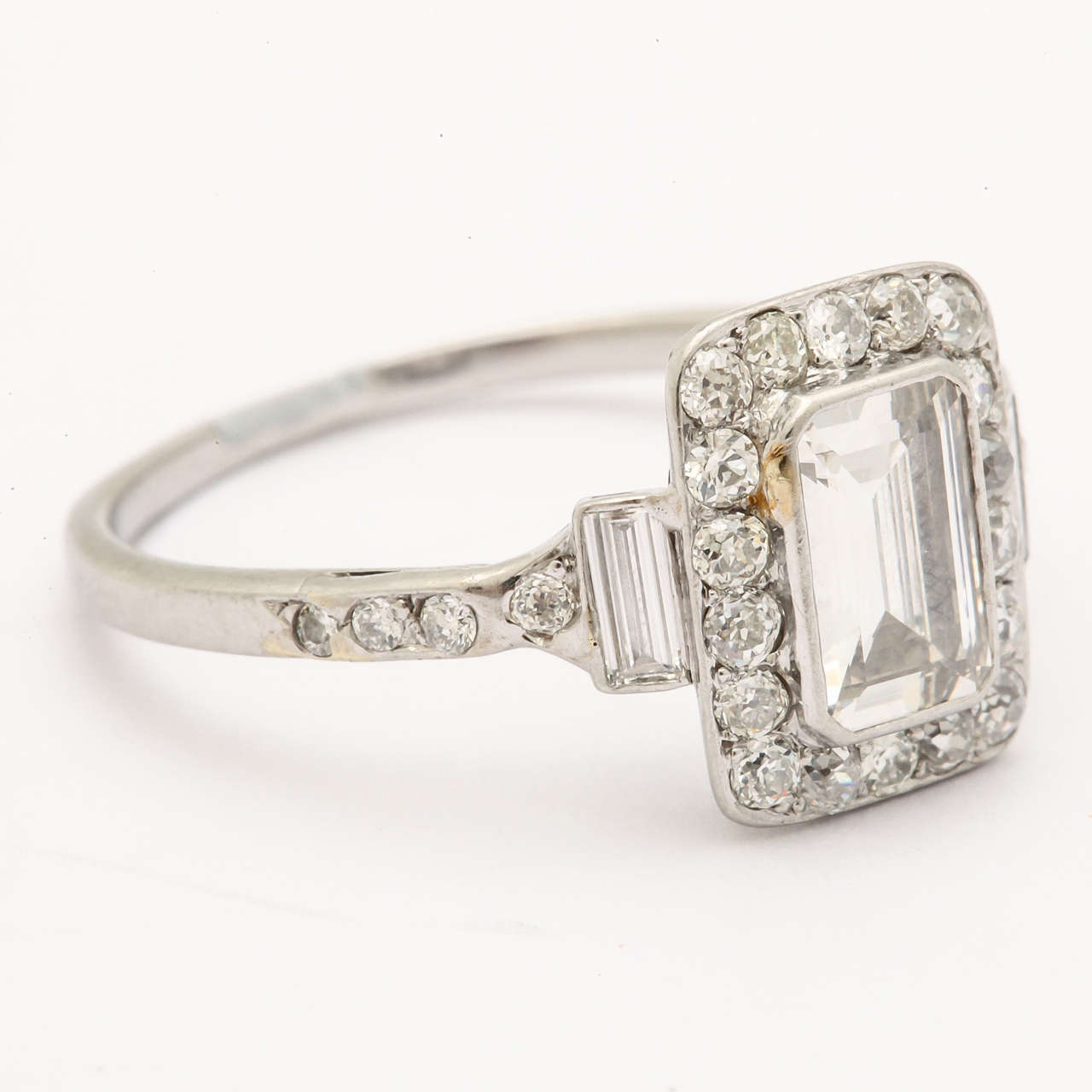 This piece has a 1.15 ct elongated emerald cut diamond surrounded by 18 round diamond and 2 baguettes on either side weighing approximately .38 ct. The diamond is an excellent quality; F color, VS 1. Interesting and beautiful as an engagement ring.