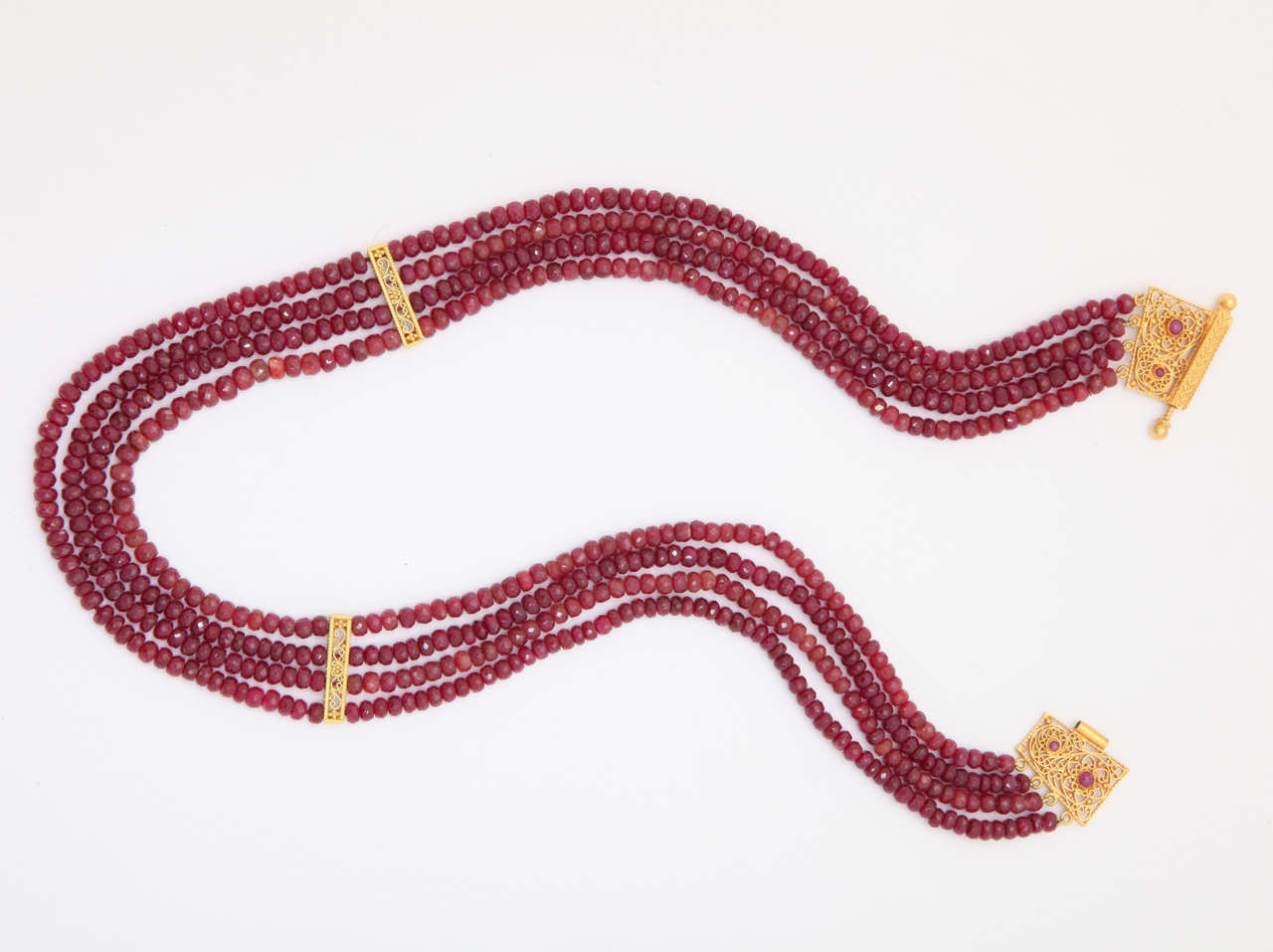 This 4 strand faceted ruby bead necklace is elegant and classic. The four strands are separated  by 18 kt  hand made wire scroll dividers. The spectacular, also hand made, clasp is 18 kt with ruby cabs. The clasp opens with a central screw. The