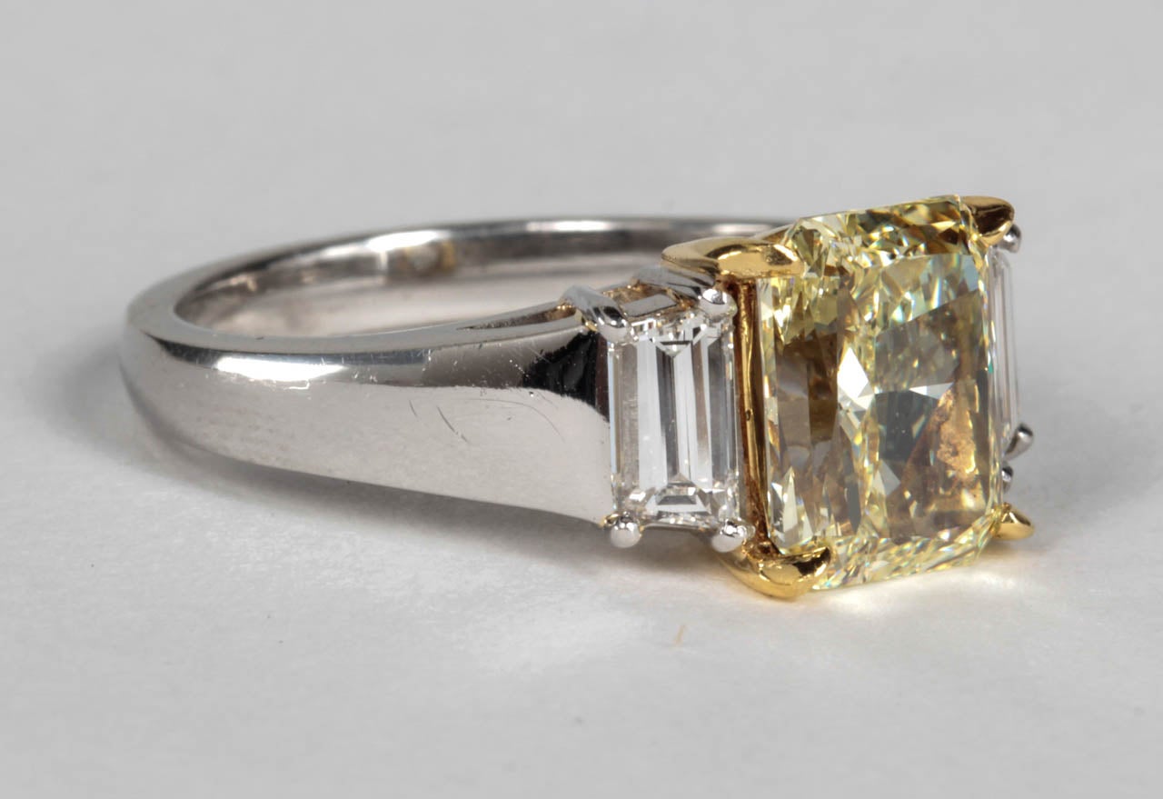 2.86 carat GIA certified Radiant cut center Fancy Light Yellow diamond, VS2 clarity. 

The center diamond is set with white step cut trapezoid diamonds weighing .75 carats -- VS clarity. 

The ring is custom made in platinum and 18k yellow gold.