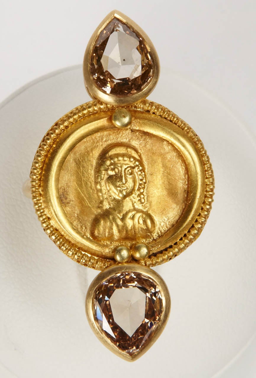 Gold cast and chiseled button depicting a facing praying lady, within a lunar crescent motive, with two and one large beads, within a fine beaded rim, Roman Art from the 4th century, set on an 18K mat gold ring, enhanced with two attractive Fancy