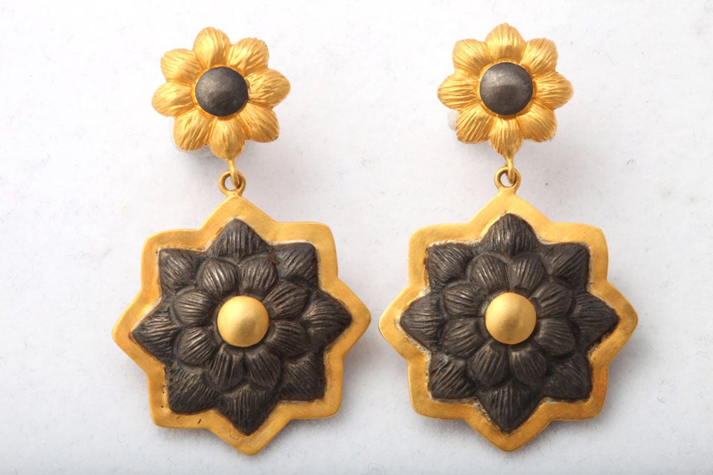A pair or 18kt yellow gold and rhodium plated sterling silver sunflower earrings. The earrings are each composed of two flowers. An 18kt yellow gold flower stud with a rhodium plated sterling silver center suspends a larger rhodium plated sterling