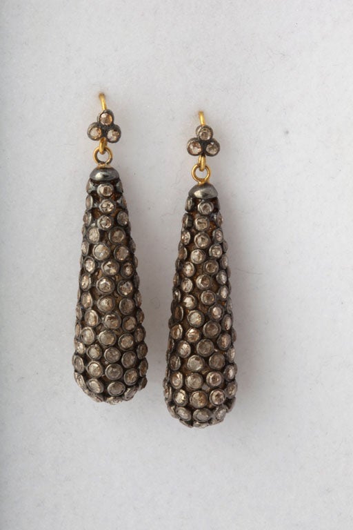 A pair of diamond bezel set drop earrings. The earrings are suspended from diamond bezel set clusters on 18kt yellow gold hooks.