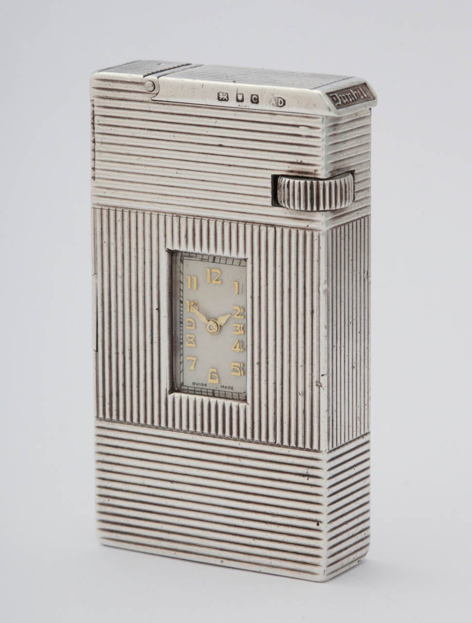 Sterling silver Dunhill Broadboy lighter with watch. Ribbed design with integral watch. Watch has a silvered dial with Arabic numerals. Marked Dunhill with silver hallmarks. 1938. 
Dimensions are 58mm / 32mm / 12mm.