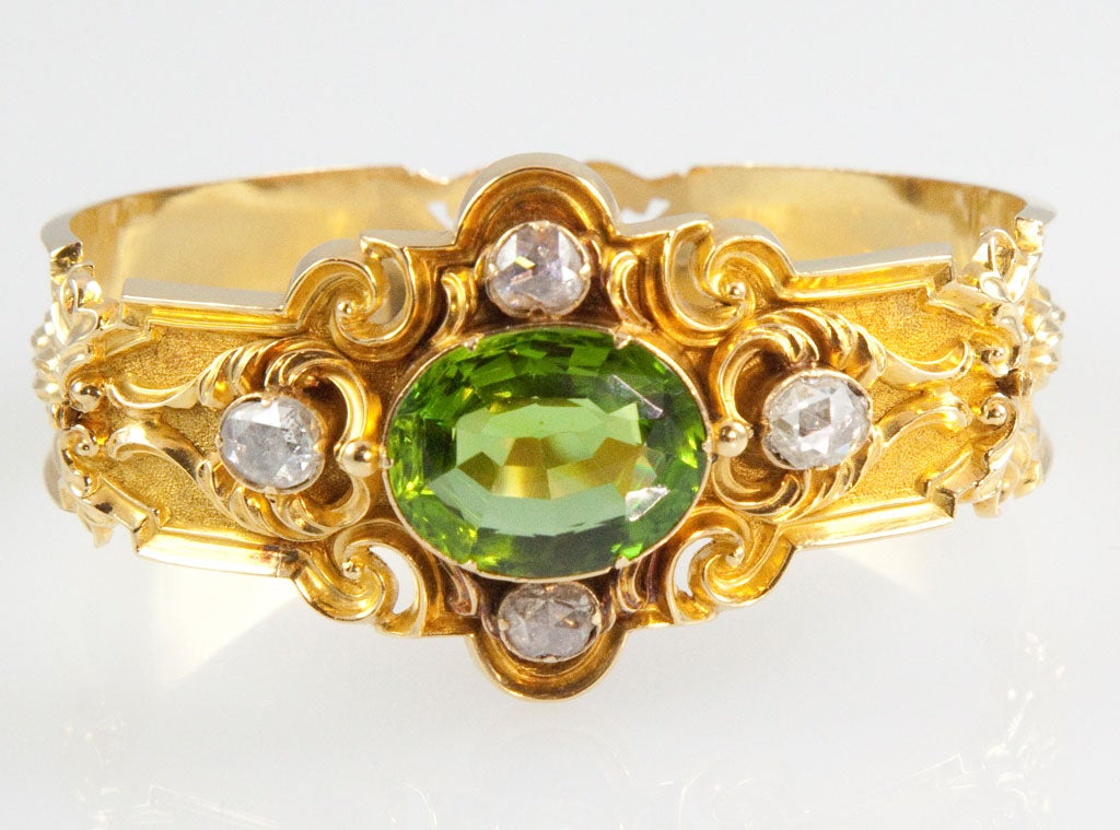The back of the bracelet is done in repousse with graduated size flowers on bloomed gold. The top of the bracelet centers 1 large faceted peridot surrounded by 4 rose-cut diamonds. Peridot: 20.30 carats, diamonds: 1.77 carats.