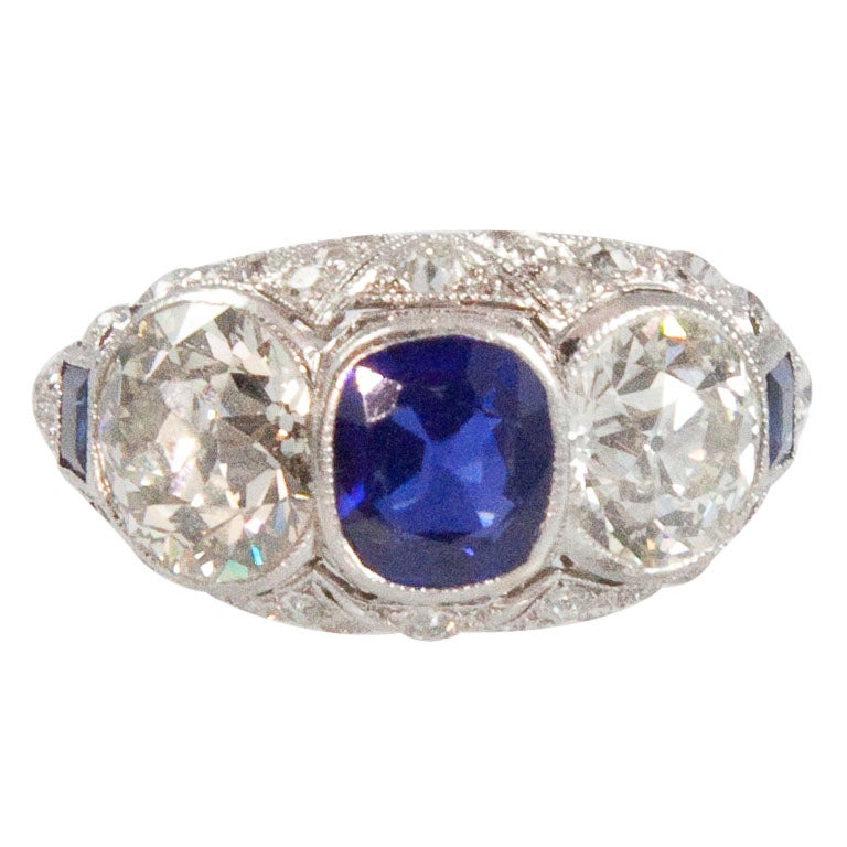 The ring is bezel-set with 2 old European-cut diamonds, 2.40 carats and 2.05 carats, color: I-J, clarity: VS1-VS2, the center bezel-set with 1 faceted blue sapphire 1.45 carats. Beautiful work and craftmanship with exquisite detail throughout the