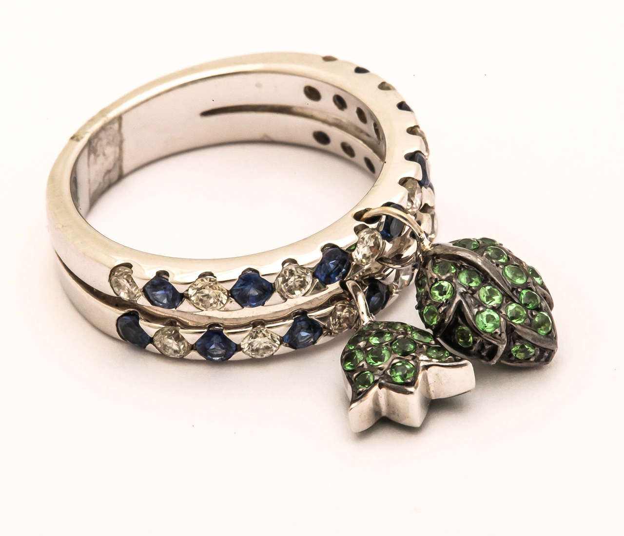 This dynamic ring has moving parts. The tulip and leaf are pave set with green garnets and are flexibly attached to the  sapphire and diamond set band rings. The bands are one unit, that is, joined together at the  back of the ring shank. The ring