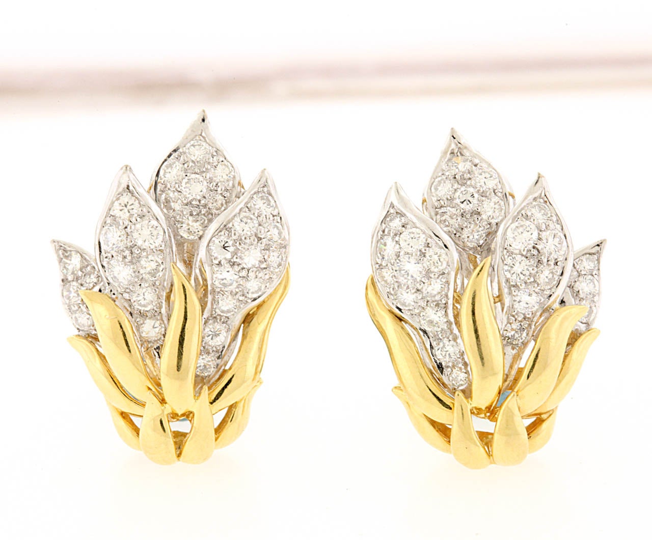 Diamond flame earrings, circa 1980's, are set with diamond pavé stylized leaves rising from 18K yellow gold petals, all in 18K gold, measuring 1/2
