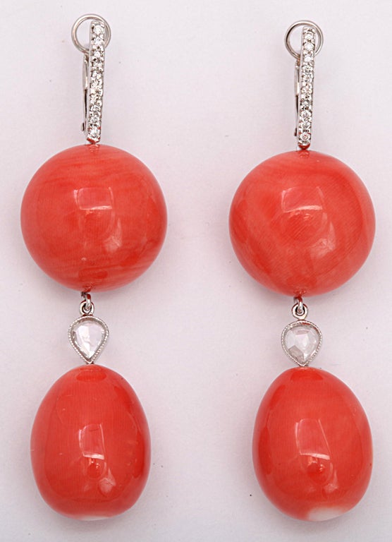 A pair of coral earrings composed of button and oval coral beads which are separated by 18kt white gold bezel set rose cut diamonds. The earrings are suspended by 18kt white gold and diamond clips.