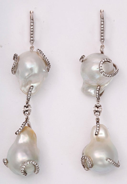 A pair of baroque pearl earrings composed of double drop baroque pearls which have been wrapped in 18kt white gold and diamond waves and they are separated by diamond clusters. The pearls are suspended by 18kt white gold and diamond clips