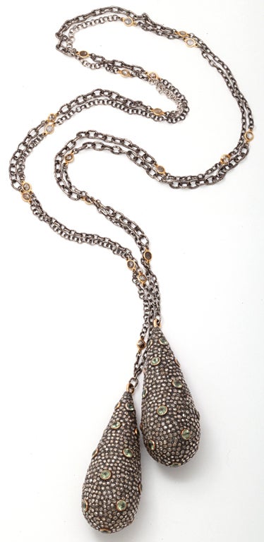 A lariat composed of two sterling silver drop beads which are set with pale green sapphires bezel set in 18kt yellow gold and pave set diamonds. The two beads are attached to a sterling silver chain which has been scattered with rose cut diamond set